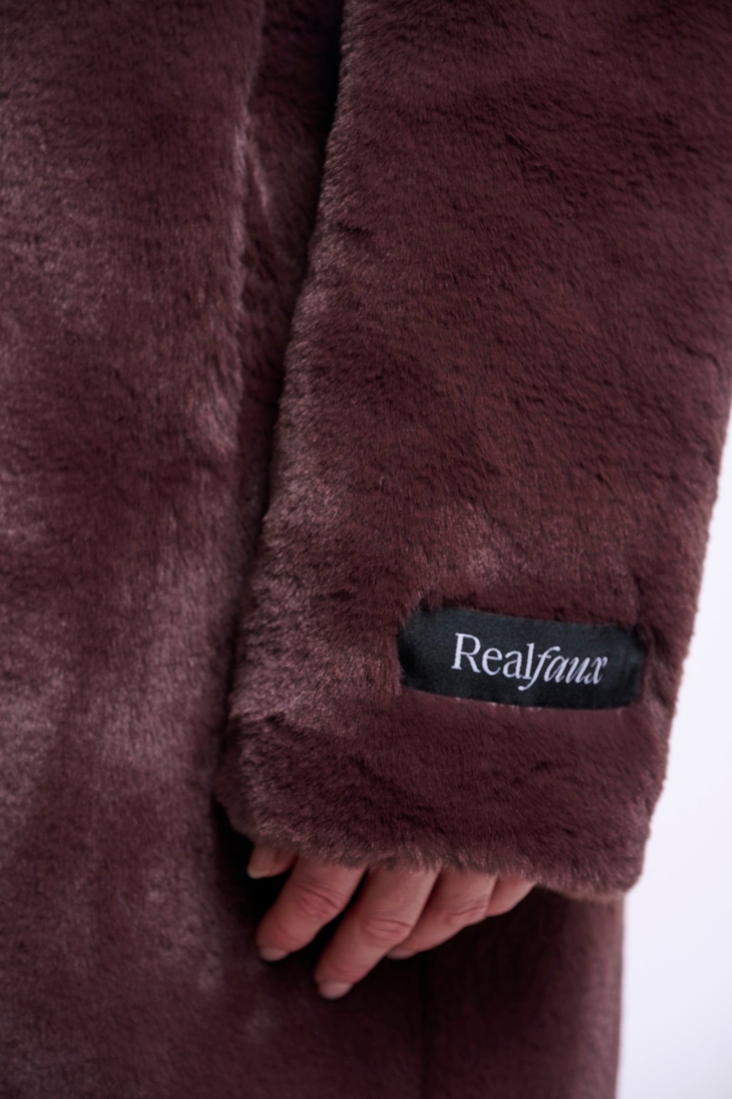 Close-up of a brown faux fur coat with 'Realfaux' label on a white background