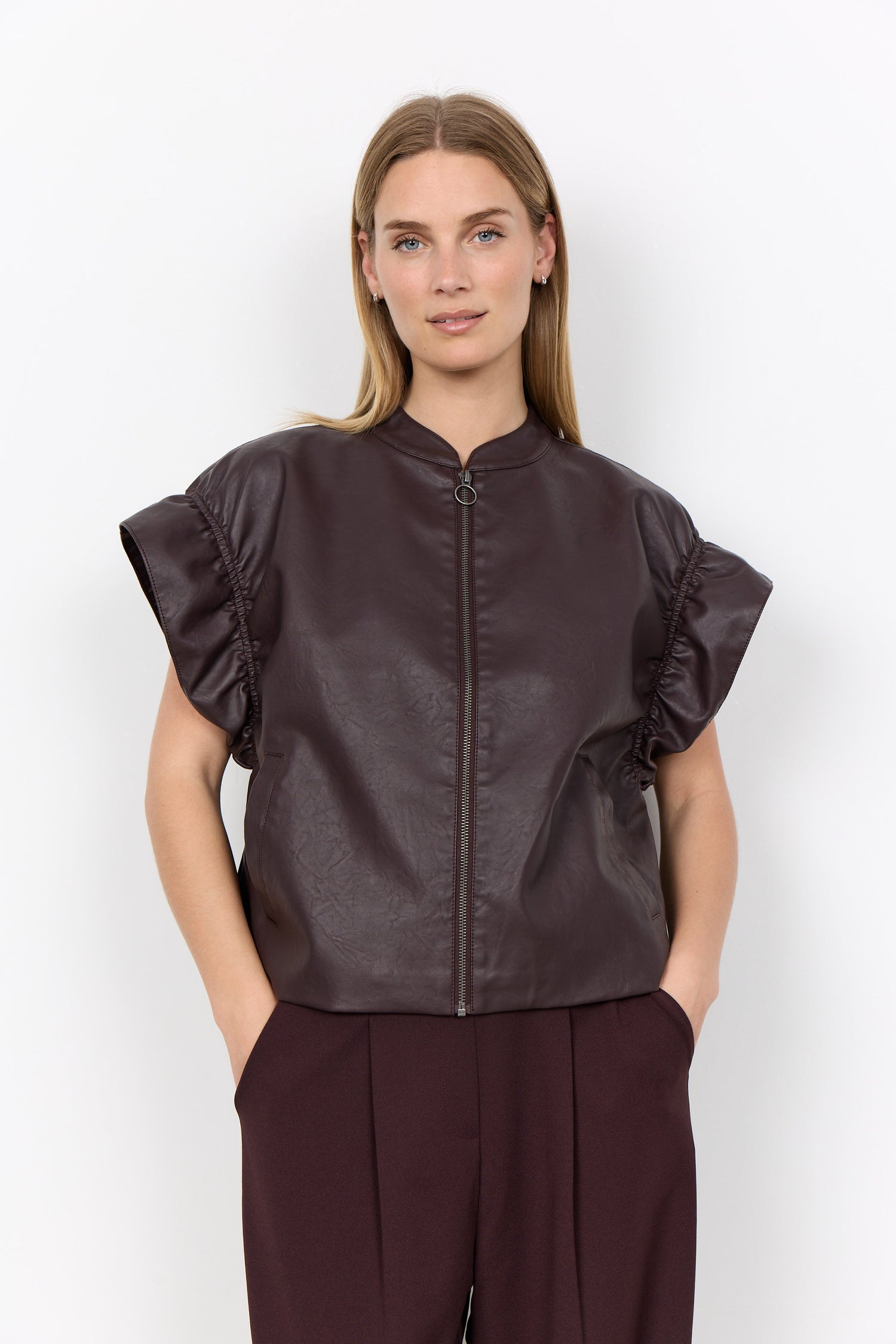 Woman wearing a dark brown leather jacket with ruffled sleeves on a white background