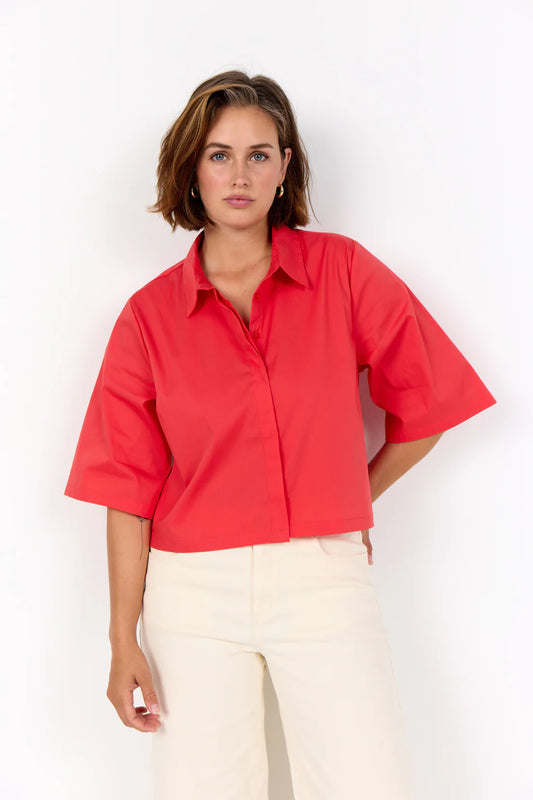 Woman wearing a red shirt and white pants against a white background