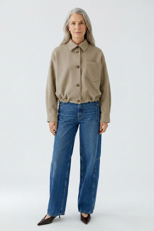 Woman wearing a beige jacket and blue jeans on a white background