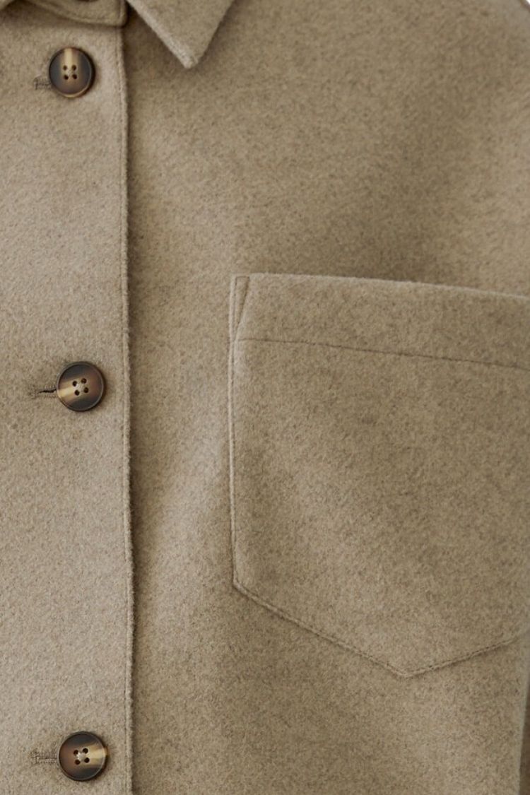 Close-up of a beige coat with button details and a pocket.