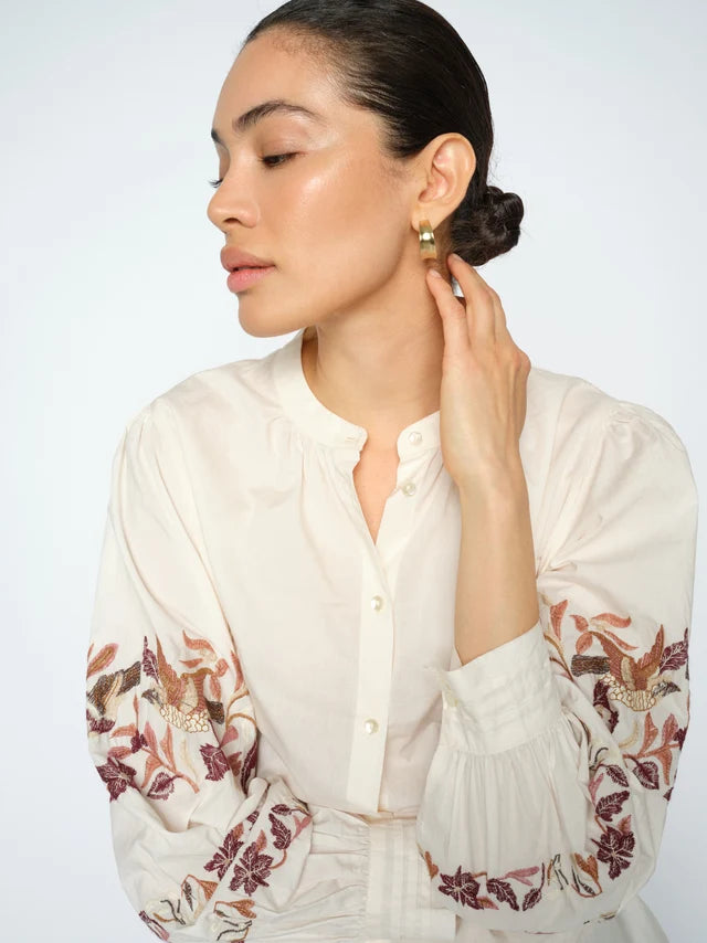 Woman wearing a white blouse with floral patterns on a plain background