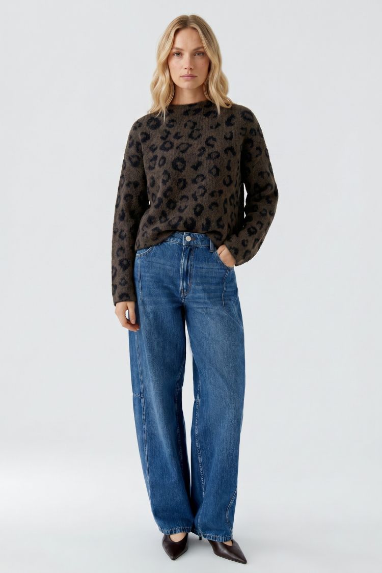 Woman wearing a dark leopard print sweater and blue jeans on a light gray background
