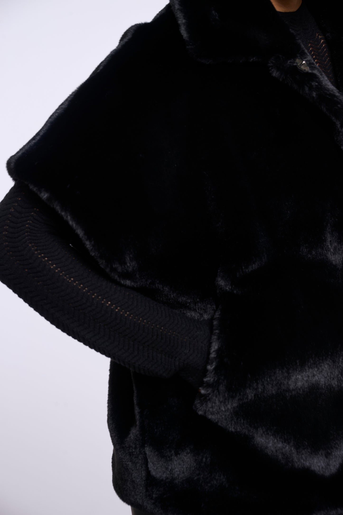 Close-up of a black faux fur jacket with a ribbed knit sleeve and collar, shown on a mannequin against a light gray background.