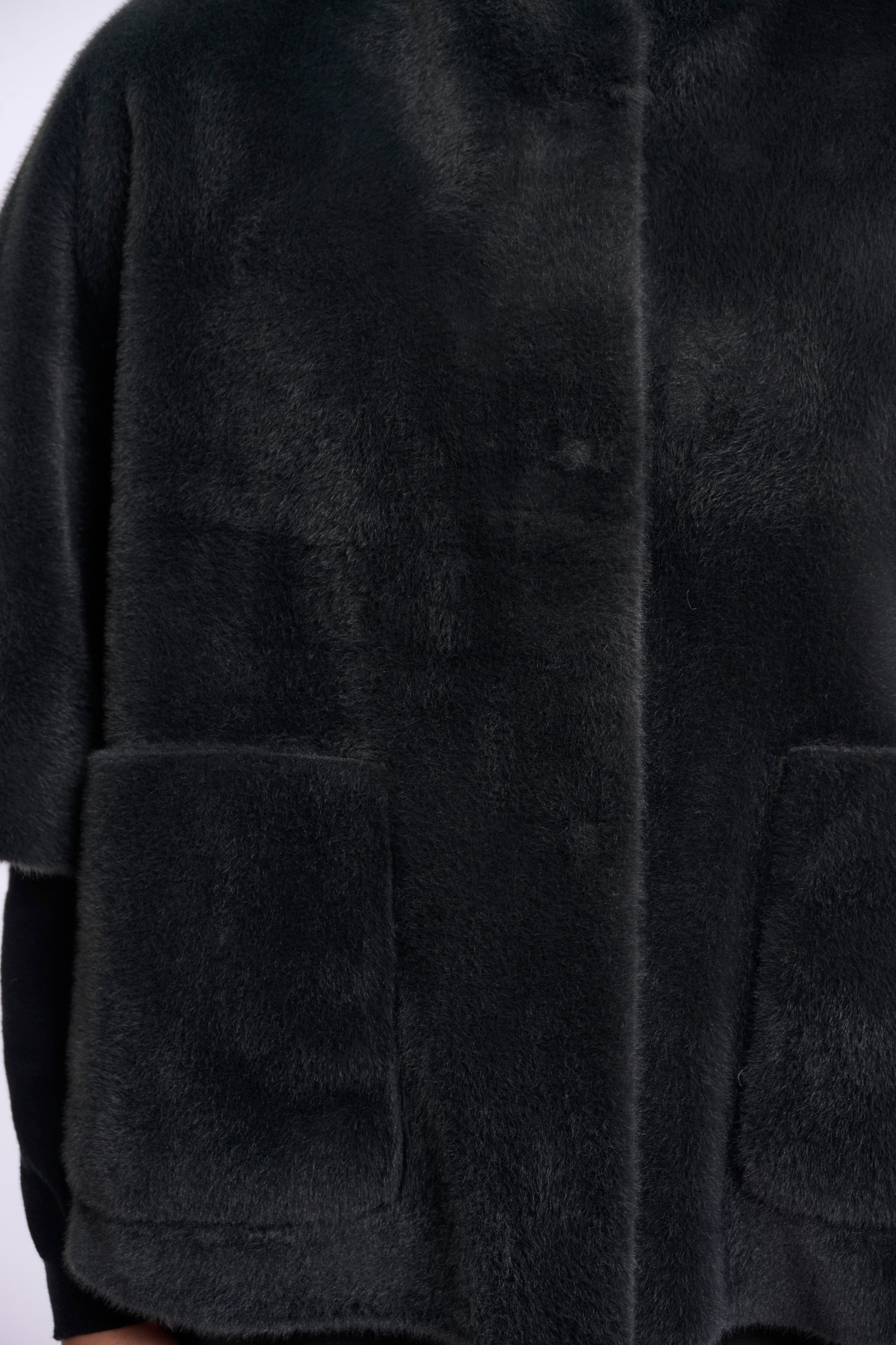 Close-up of a black plush faux fur jacket with a button closure and two front patch pockets.