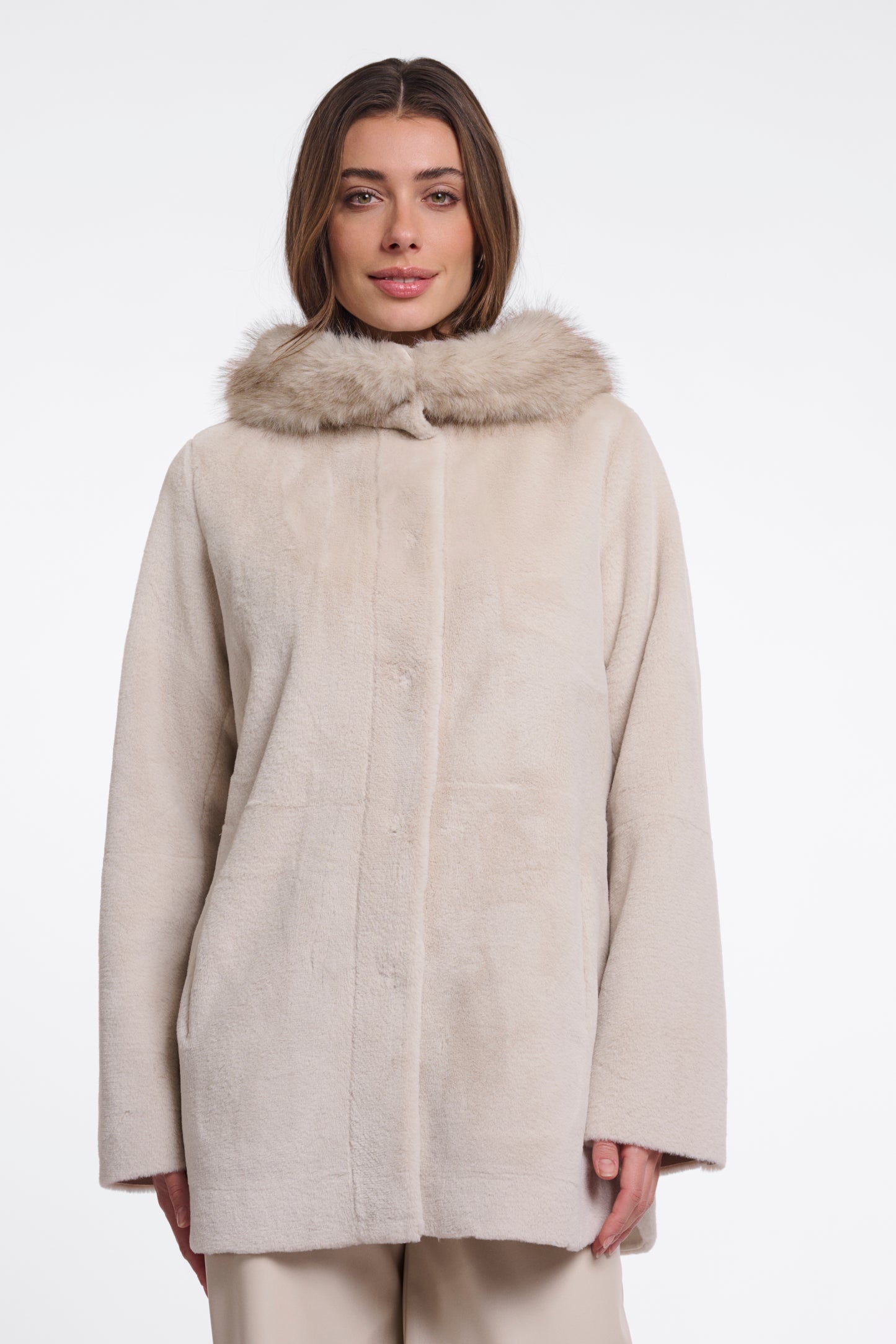 A woman wearing a light beige faux fur coat with a matching faux fur collar, photographed against a plain white studio background.