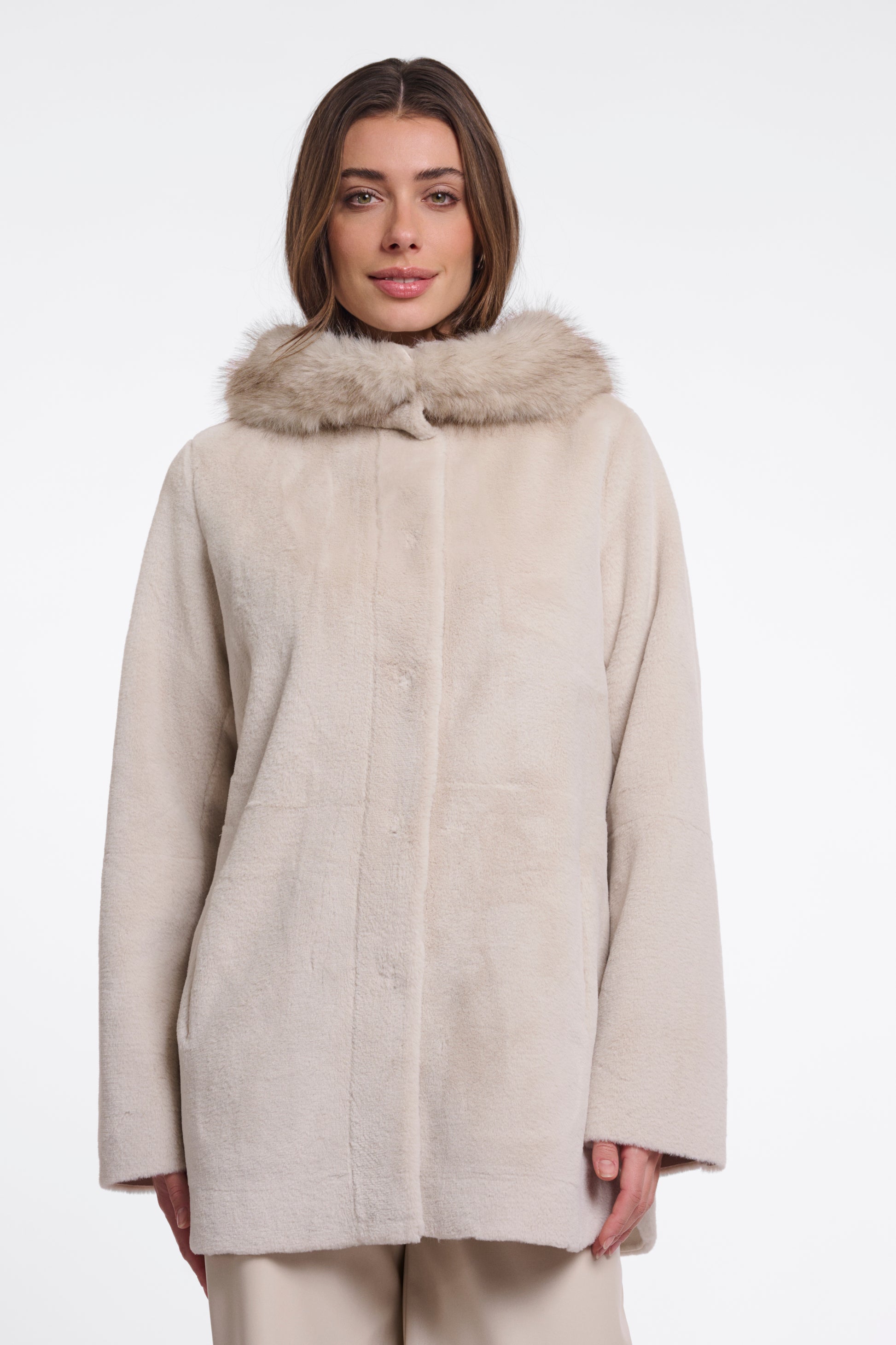A woman wearing a light beige faux fur coat with a matching faux fur collar, photographed against a plain white studio background.