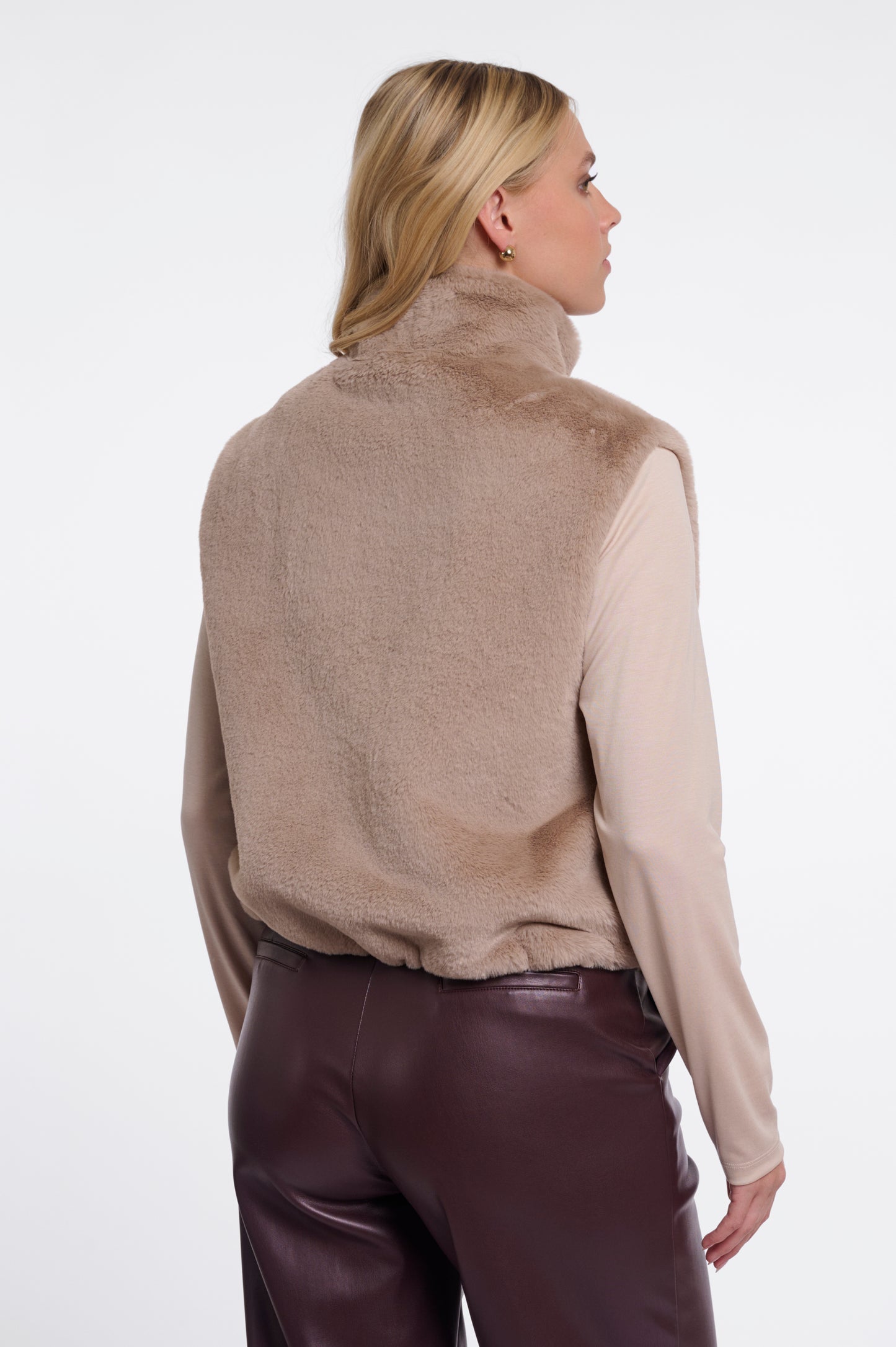 Person wearing a beige turtleneck sweater and purple pants on a white background
