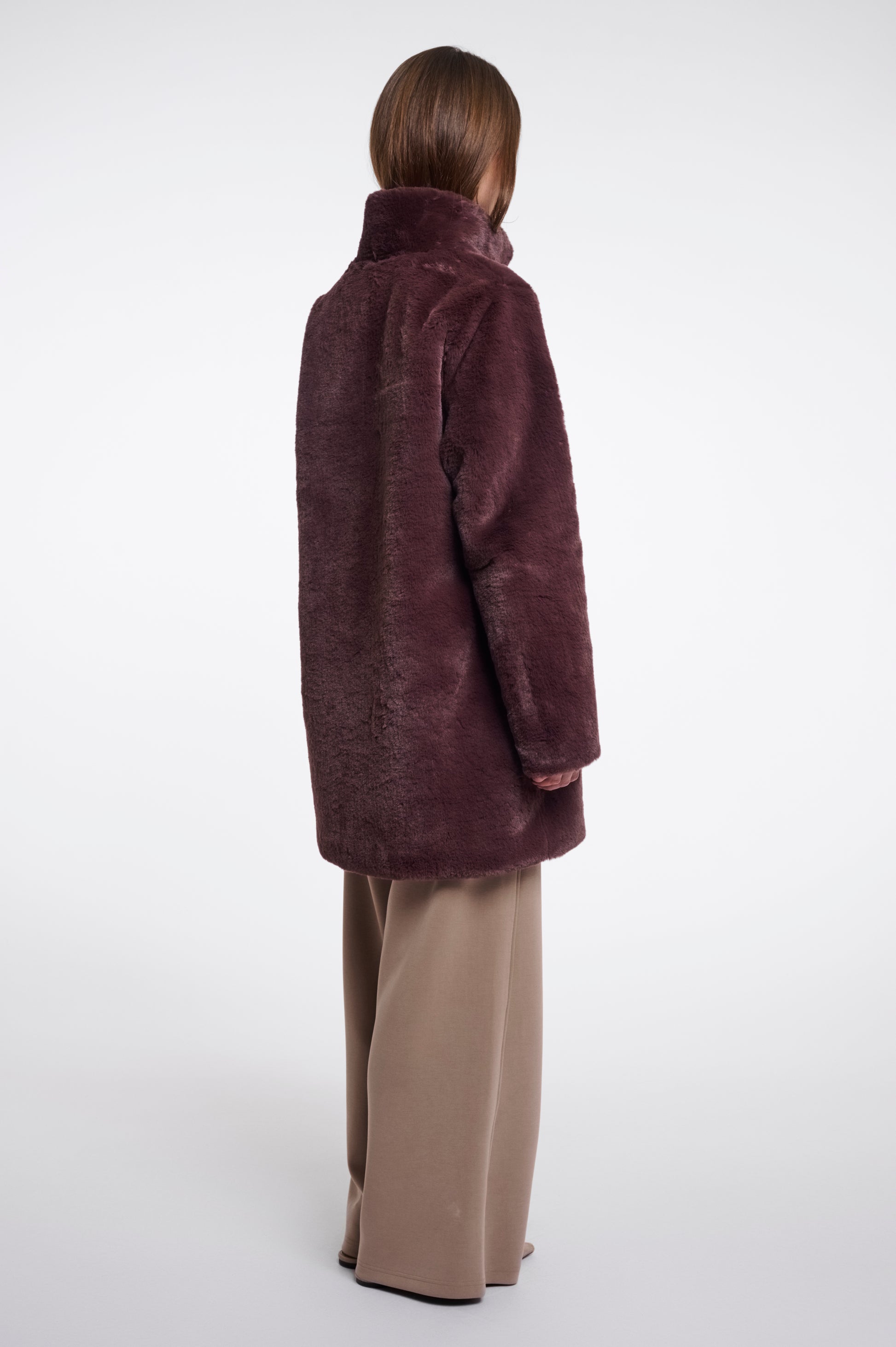 Person wearing a brown coat and beige pants on a white background
