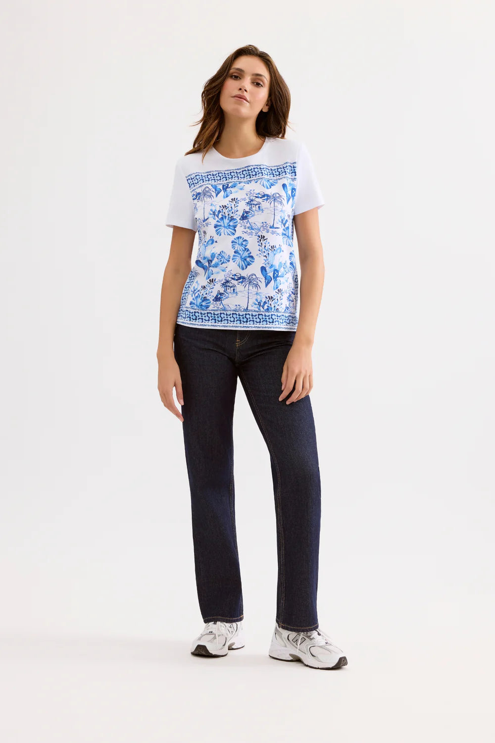 Woman wearing a white t-shirt with blue floral pattern and dark jeans on a white background